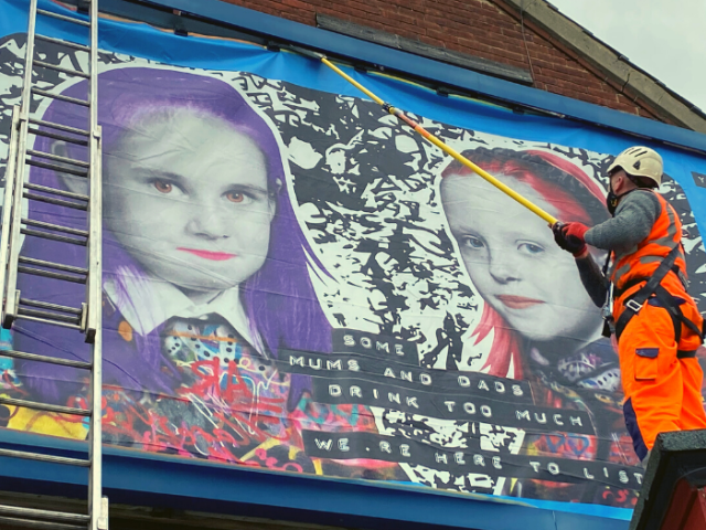 Large poster of the #heretolistencampaign being put up on the side of a building