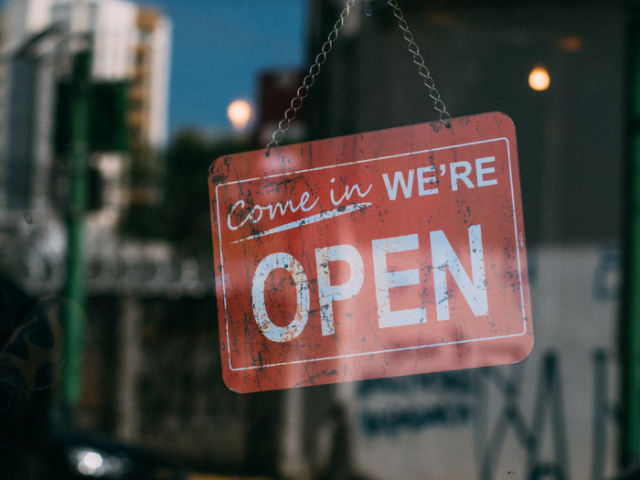 A picture of a glass door with a sign reading 'we are open'