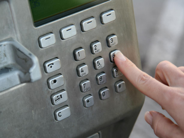 Dialling pad inside a phone box with finger pressing one of the buttons