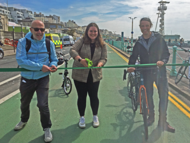 A picture of three people cutting a ribbon on a green cycle lane