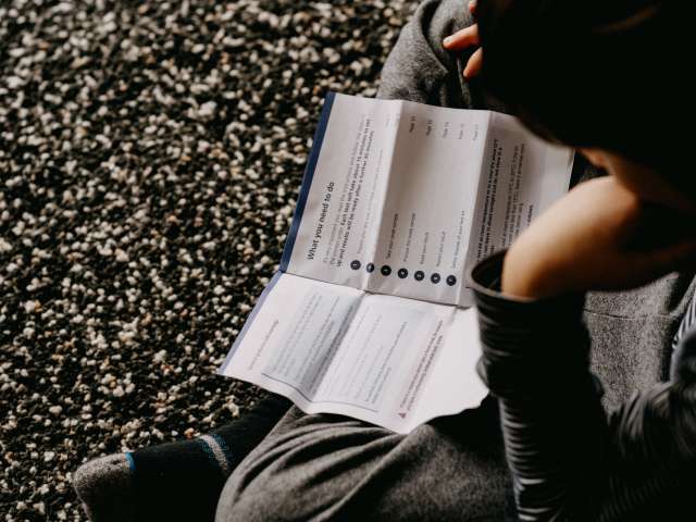 Person sitting cross legged on pebbles reading Covid-19 self test instructions. Photo by <a href="https://unsplash.com/@anniespratt?utm_source=unsplash&utm_medium=referral&utm_content=creditCopyText">Annie Spratt</a> on <a href="https://unsplash.com/s/photos/covid-test?utm_source=unsplash&utm_medium=referral&utm_content=creditCopyText">Unsplash</a>
  