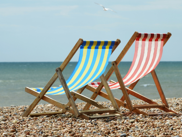 A pair of deckchairs, one blue and white stripes, one red and white stripes, on the pebbles of Brighton beach