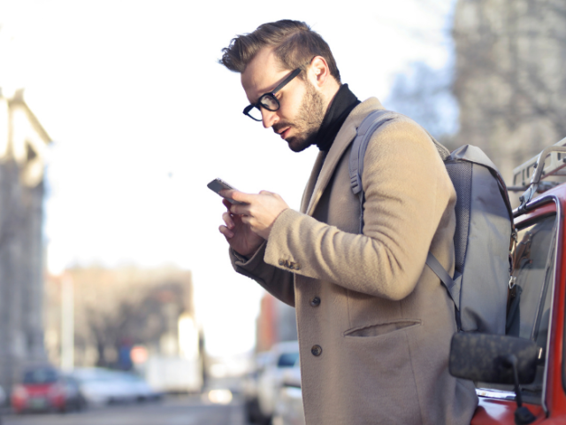 A man leaning against a car looking at his mobile phone