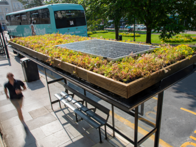 A picture of a bus shelter with flowers and a solar panel on the roof