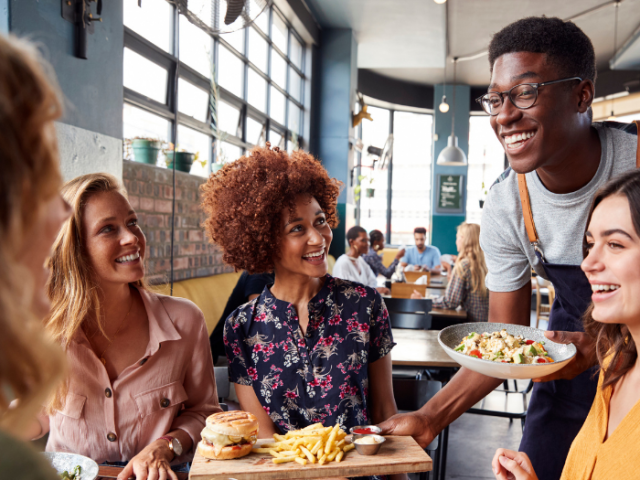 four young women having lunch in a restaurant being served by a man