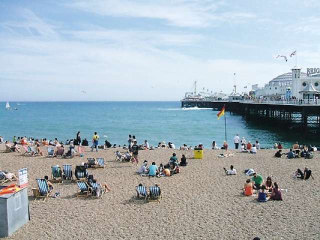 People sitting on the beach with Palace Pier in the background.