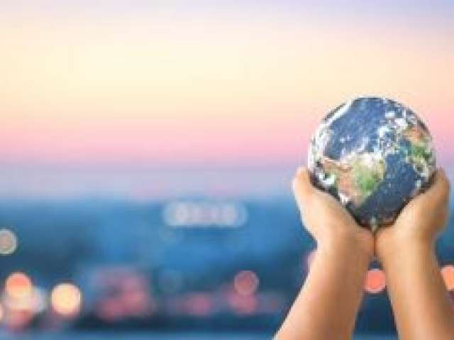 Image of a two hands holding a the planet Earth in front of a a city scene during