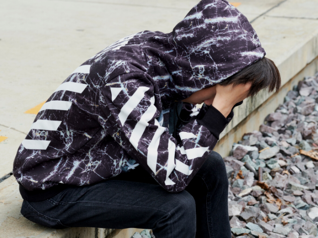 teenager sat on a pebble beach with his head in his hands