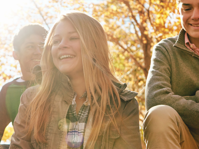 Three teenagers sitting in the sunshine in front of a tree