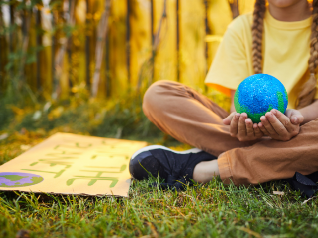 child sat cross legged on the grass holding a model of the world