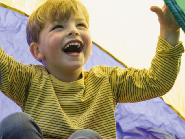 Smiling small child plays inside a multi-coloured play tent