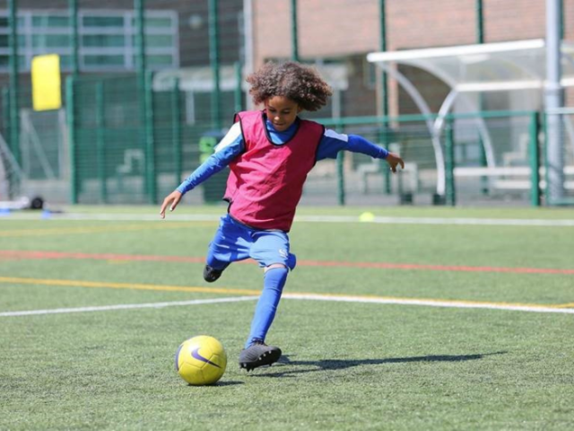 A child of about nine plays football on a grassed pitch in Albion kit