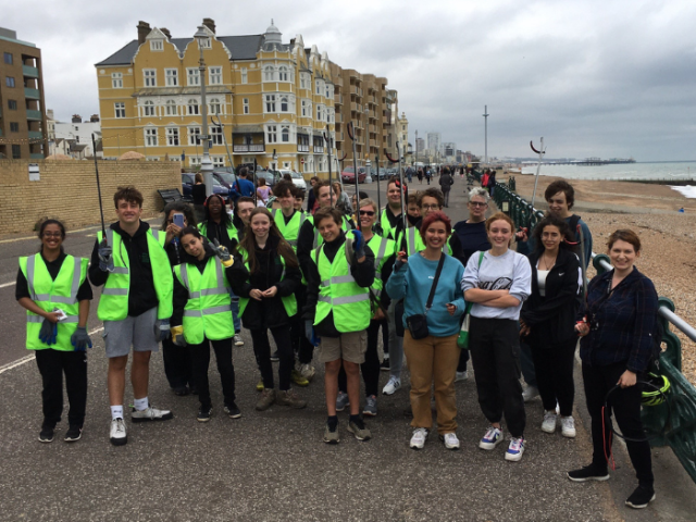 A large group of young people in hi vis pose with the council deputy leader by a Brighton beach 