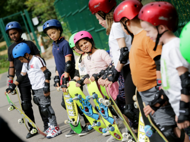 A group of children stand holding skateboards and wearing helmets