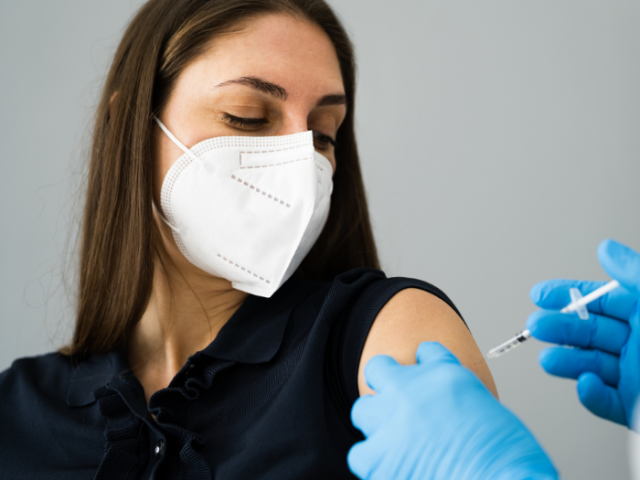 Woman with brown hair and wearing a face covering getting a vaccination