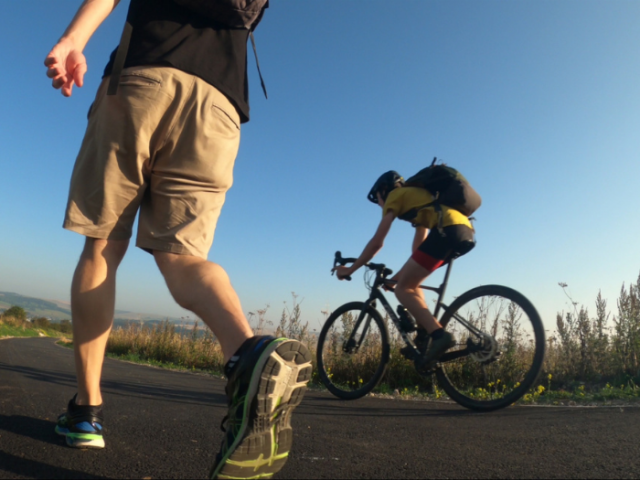 A picture of a two people, one walking and the other cycling