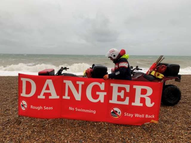 A quad bike on the beach behind a red danger sign with stormy seas in the background