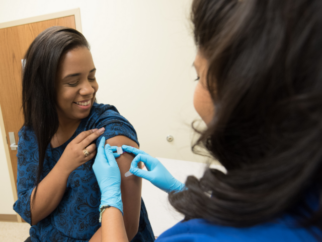 Woman has a small sterile dressing applied to her left upper arm by a female medic after receiving a vaccination