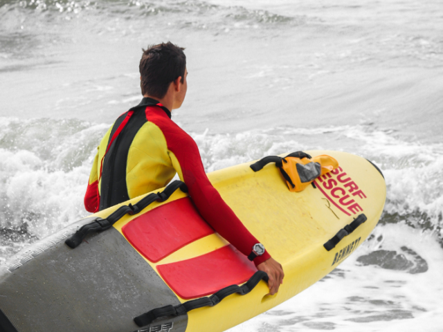 Picture of a lifeguard carrying a surfboard into the sea