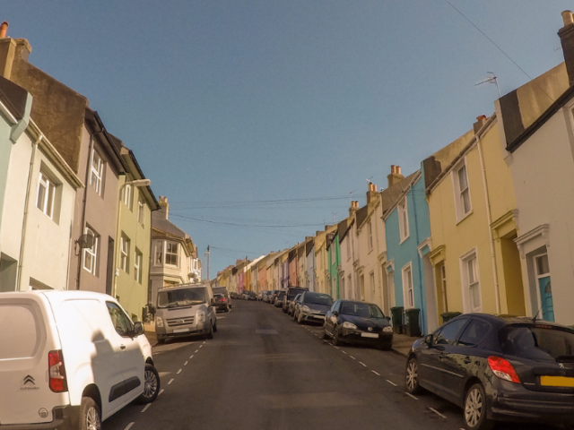 A picture of a road with houses and cars either side