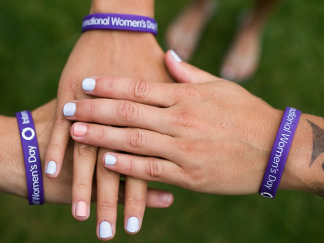 Photo of three women's hands together with International Women's Day bracelets on their wrists.