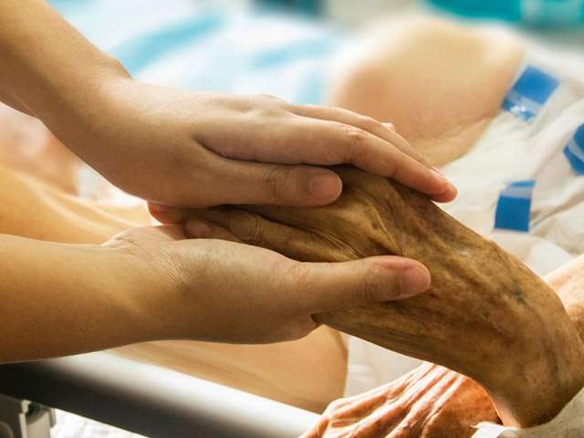 An image of a health care worker holding hands with an elderly person. 