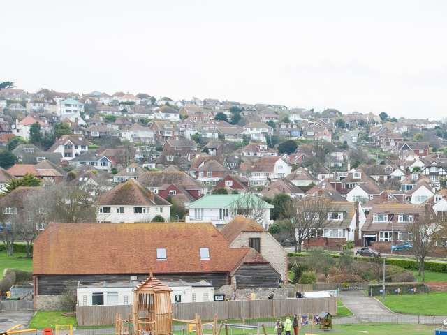 A view of Saltdean taken from Saltdean Oval Park showing the playground in the foreground with houses rising up the hill filling the horizon to the sea. 