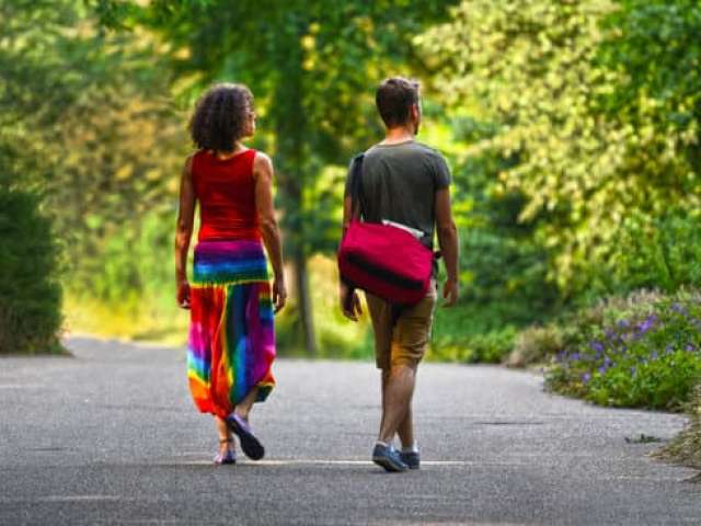 A man and woman in colourful clothing walk together in the sun on a woodland road.