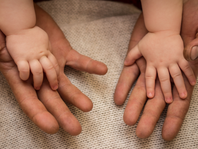 Picture of a baby's hands resting on an adult's hands 