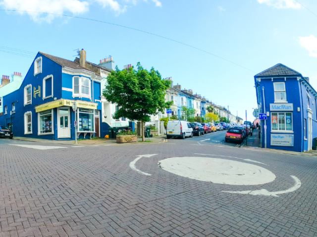 A picture of a road, with a mini roundabout and houses and shops