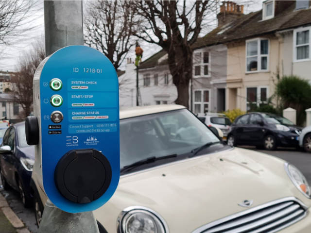 A picture of an electric vehicle lamppost charger with a car in the background