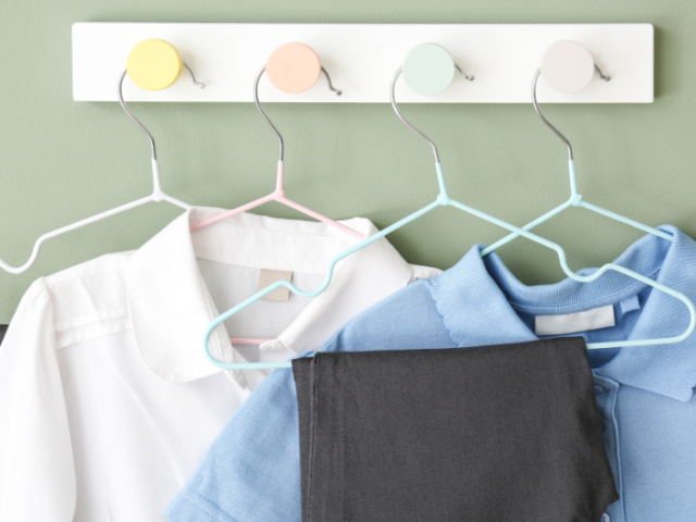 White shirt, blue shirt and grey trousers hanging on hangers from four pegs attached to a grey wall