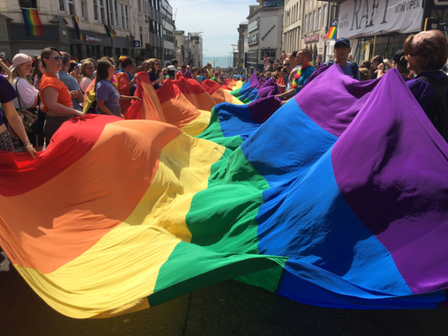 Photo of people carrying a long rainbow flag in the Pride Community Parade