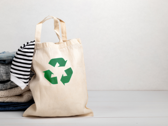organic cotton shopping bag with black and white striped sleeve spilling out of the top and a pile of folded clothes on one side