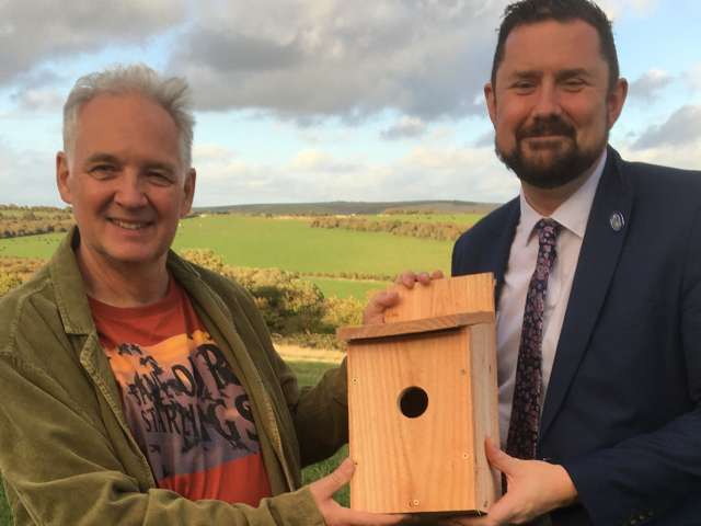 Save Our Starlings campaigner Steve Geliot with councillor Mac Cafferty holding one of the starling nest boxes with Waterhall's landscape of fields, grassland and hills in the background