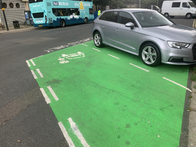 A picture of a road with a green parking bay and a car