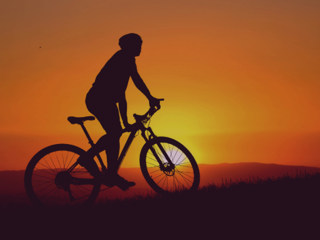 A cyclist on their bike in front of a sunset