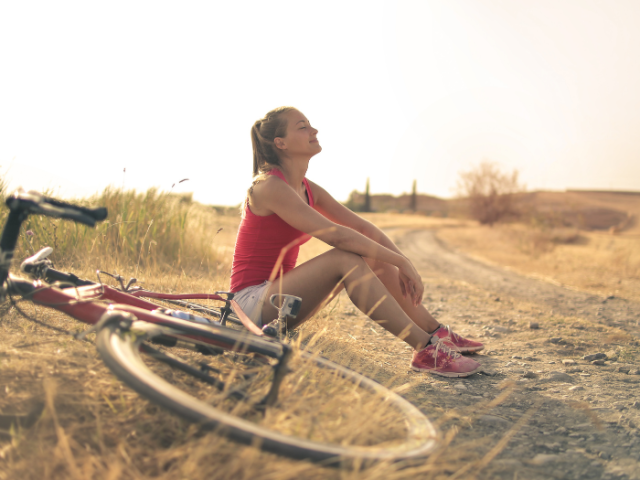 A woman sitting on the ground looking up to the sky, next to a bicycle