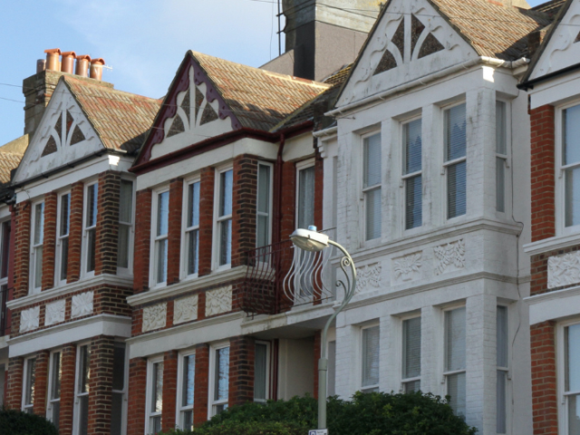 A terrace of houses in the Queen's Park conservation area. In the foreground is a lamp post and neatly clipped green hedges, behind which you can see three terraces houses. The nearest house is painted white but the other two are of red brick with white window frames and brickwork detailing.