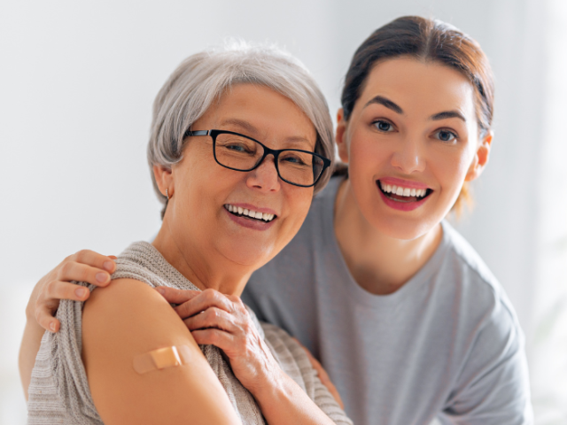 Older woman in glasses with a plaster on her arm next to a younger woman in a grey tshirt