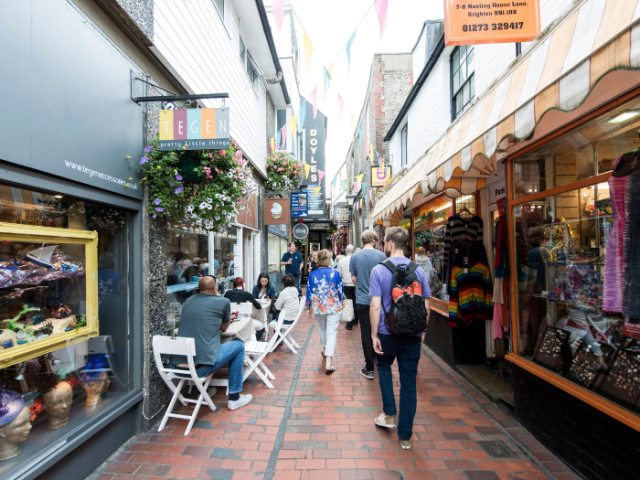 A small street with shops either side and people walking and sitting outside the shops