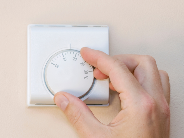 Photo of a hand adjusting a central heating thermostat