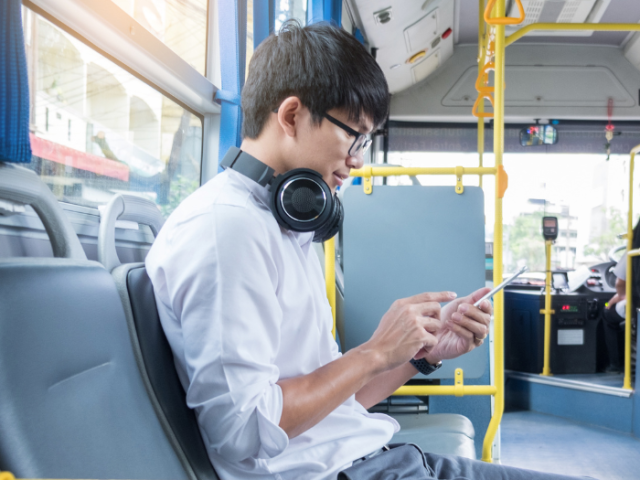 A young man sitting on a bus looking at his phone