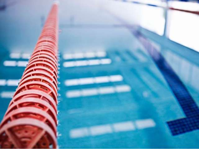 An empty indoor swimming pool with a red lane marker to the left stretching out in front of the camera
