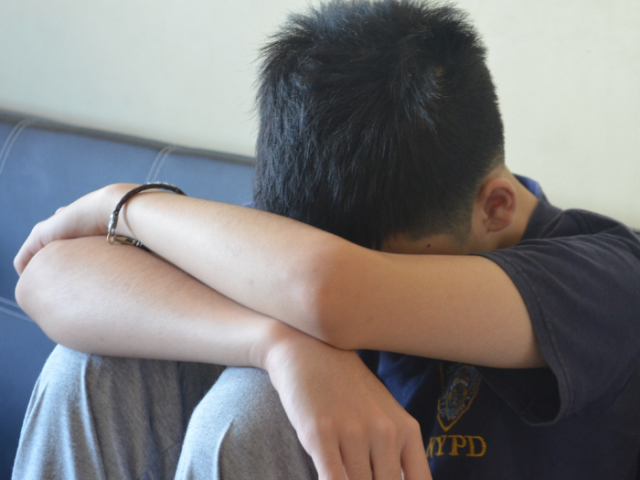 The image shows a teenage boy sat covering his face.