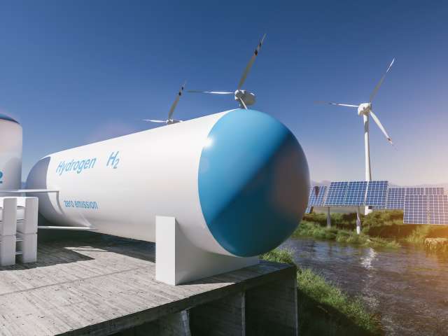 Lozenge-shaped hydrogen storage unit with hydrogen drum on left-hand side with windfarm and road in the background.