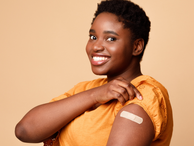 Woman in an orange top holding up her sleeve to show a plaster on her arm