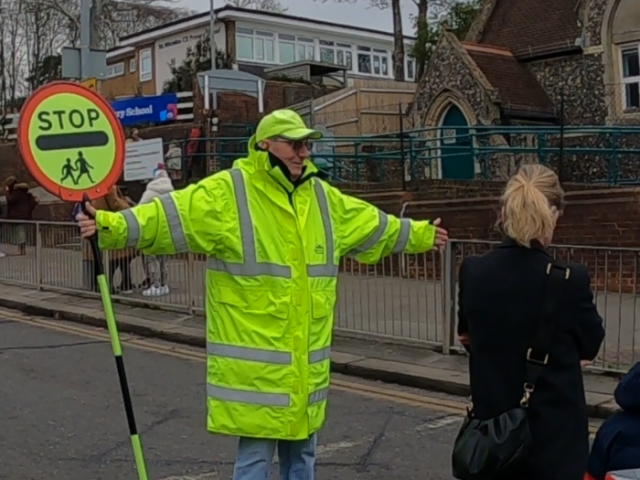 A man holding a stop, school children sign and a woman crossing a road