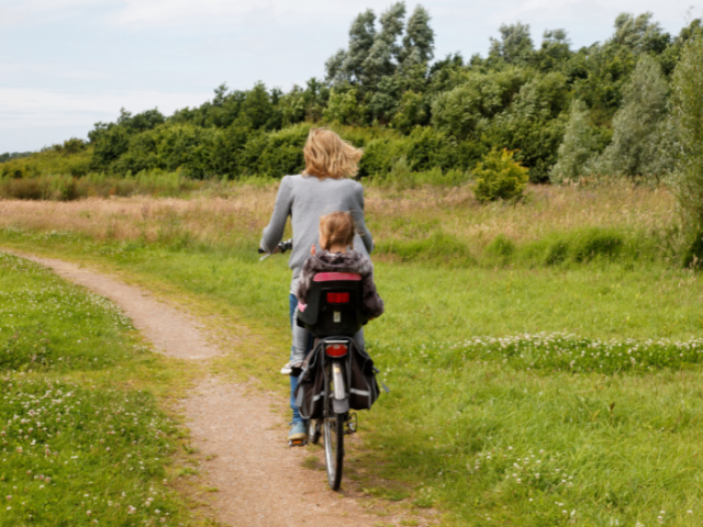 A woman cycling with a small child in a carry seat in a green and grassy area
