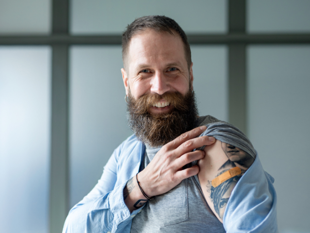 Man with his sleeve down showing tattoos and a plaster on his arm